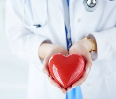 Steteskop tutan, kalbi hafif arka planda olan kadın bir doktor.
