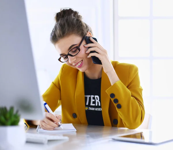 Portret van een mooie vrouw die belt terwijl ze op haar werkplek voor de laptop zit en aan een nieuw project werkt — Stockfoto