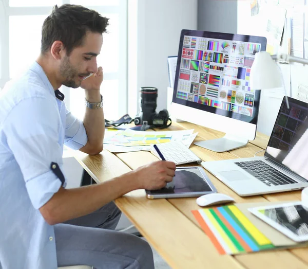 Portret van jonge ontwerper zittend in grafische studio achter laptop en computer terwijl hij online werkt. — Stockfoto