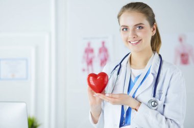 Steteskop tutan, kalbi hafif arka planda olan kadın bir doktor.