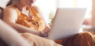 Evde dizüstü bilgisayar üzerinde çalışan kanepede oturan genç kadın