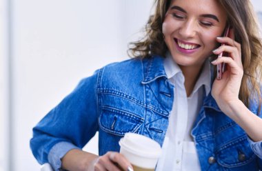 Kafede kahve içip cep telefonuyla konuşan genç bir kadın.