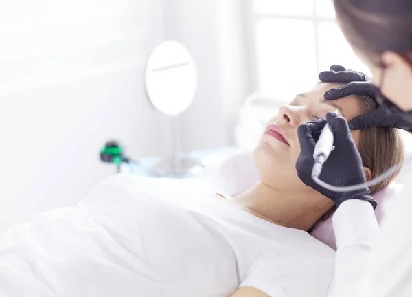 Young woman undergoing procedure of eyebrow permanent makeup in beauty salon — Stock Photo, Image