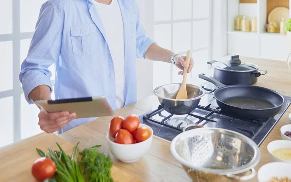 Man following recipe on digital tablet and cooking tasty and healthy food in kitchen at home — Stock Photo, Image