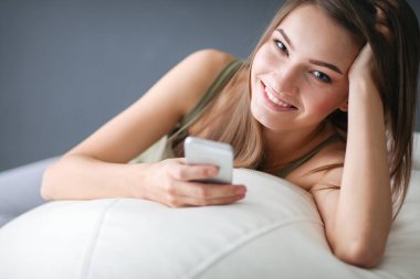 Güzel bir kadın beyaz bir kanepede bir fincan kahveyle dinleniyor.