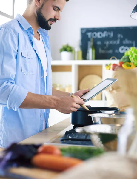Dijital tablet ve yemek pişirme tarifine uyan bir adam evdeki mutfakta lezzetli ve sağlıklı yemekler pişiriyor. — Stok fotoğraf