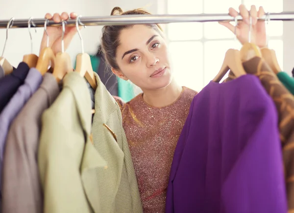 Bella giovane stilista vicino rack con appendini — Foto Stock