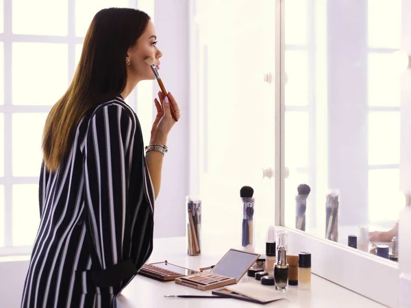 Skönhet kvinna tillämpa makeup. Vacker flicka ser i spegeln och tillämpa kosmetiska med en stor pensel — Stockfoto