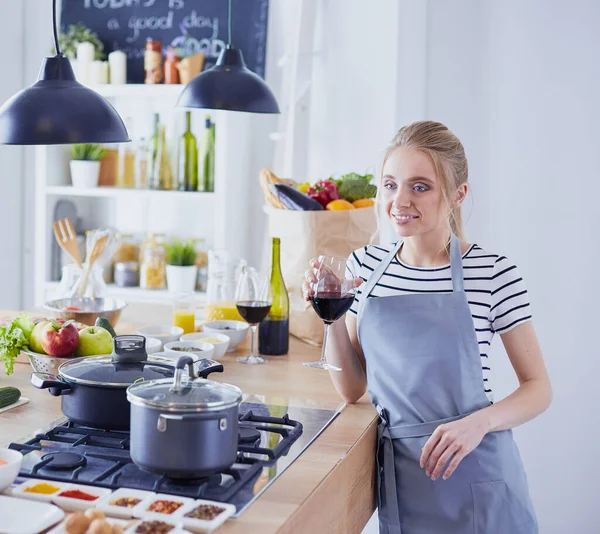 Mujer bonita bebiendo un poco de vino en casa en la cocina —  Fotos de Stock