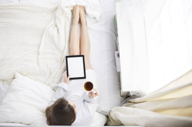 Sabahları yatakta otururken tablet kullanan ve kahve içen kadın portresi