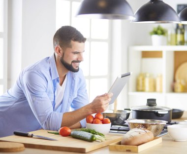 Dijital tablet ve yemek pişirme tarifine uyan bir adam evdeki mutfakta lezzetli ve sağlıklı yemekler pişiriyor.