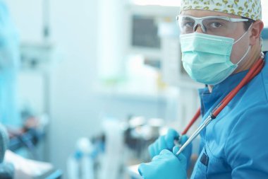 Ameliyat odasında arka planda erkek cerrah var.