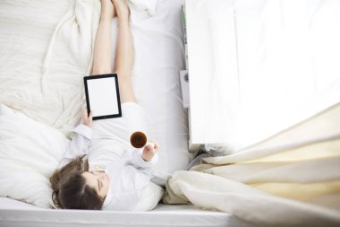 Sabahları yatakta otururken tablet kullanan ve kahve içen kadın portresi
