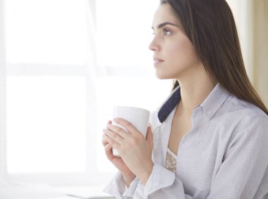 Yatakta oturup kitap okuyan ve kahvaltı yapan bir kadın.