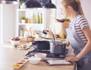 Mutfakta yemek yapmak için tablet bilgisayar kullanan genç bir kadın.