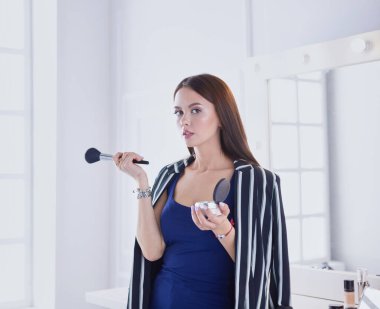 Makyaj fırçası yüzüne yakın bir kadın portresi.