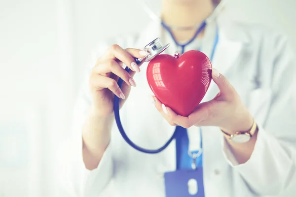 Un médico con estetoscopio examinando el corazón rojo, aislado sobre fondo blanco — Foto de Stock