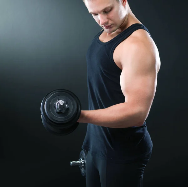 Nahaufnahme eines muskulösen jungen Mannes, der Gewichte auf dunklem Hintergrund stemmt — Stockfoto