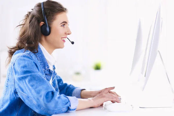 Gelukkig charmant jonge vrouw zitten en werken met laptop met behulp van headset in het kantoor — Stockfoto