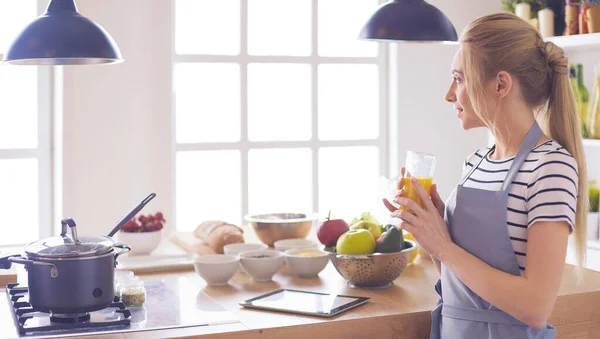 Atractiva mujer sosteniendo un vaso de jugo de naranja mientras está de pie en la cocina —  Fotos de Stock