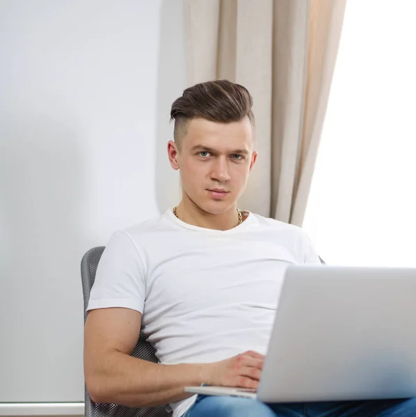 Hezký mladý muž sedí a pracuje na notebooku — Stock fotografie