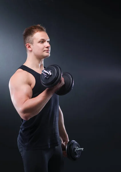 Närbild av en muskulös ung man lyfta vikter på mörk bakgrund — Stockfoto