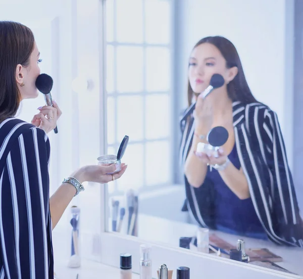 Mujer de belleza aplicando maquillaje. Hermosa chica mirando en el espejo y la aplicación de cosméticos con un cepillo grande —  Fotos de Stock