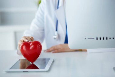 Steteskop tutan, kalbi hafif arka planda olan kadın bir doktor.