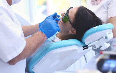 Erkek dişçi hastalarının dişleriyle uğraşıyor.