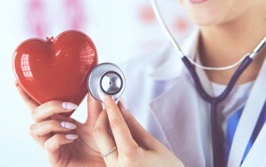 Steteskop tutan, kalbi hafif arka planda olan kadın bir doktor.