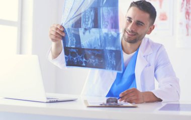 Yakışıklı doktor genç bayan hastasıyla konuşuyor ve ofisinde otururken notlar alıyor..