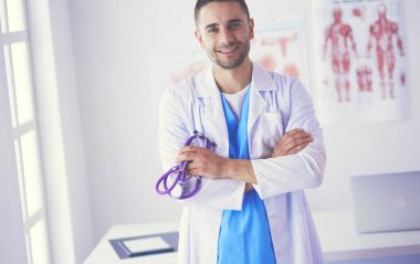 Genç ve kendinden emin erkek doktor portresi tıp ofisinde duruyor..