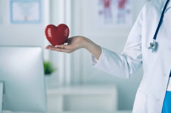 Doctora con estetoscopio sosteniendo el corazón, sobre fondo claro — Foto de Stock