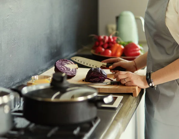 Mujer joven cortando verduras en la cocina de pie cerca del escritorio — Foto de Stock