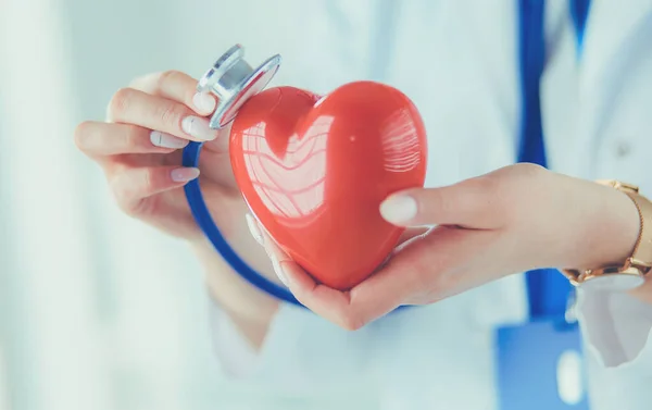 Un médico con estetoscopio examinando el corazón rojo, aislado sobre fondo blanco —  Fotos de Stock