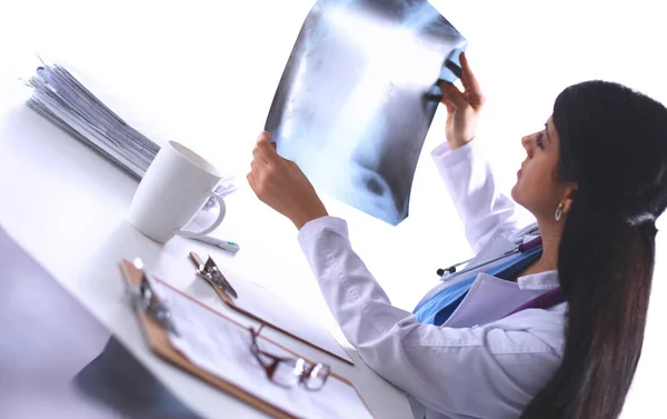 Młoda lekarka badająca zdjęcie rentgenowskie, siedząca przy biurku — Zdjęcie stockowe