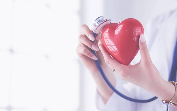 白い背景に隔離された赤い心臓を調べる聴診器を持つ医者 — ストック写真