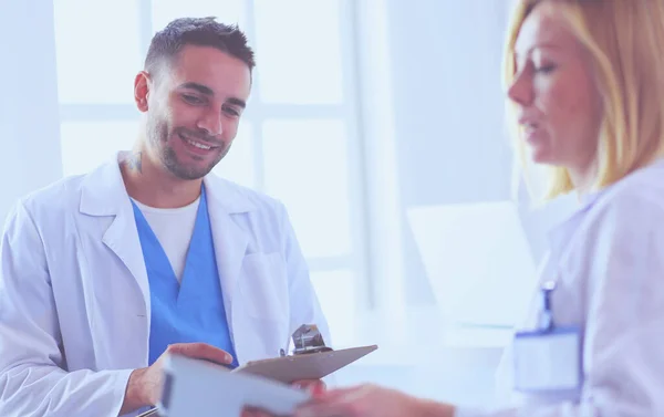 Schöner Arzt spricht mit junger Ärztin und macht sich Notizen, während er in seinem Büro sitzt. — Stockfoto