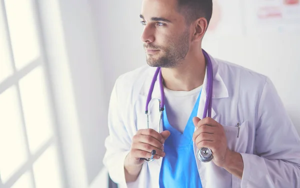 Retrato médico masculino joven y confiado de pie en el consultorio médico. — Foto de Stock