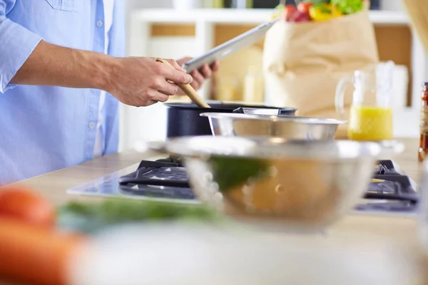 L'uomo segue la ricetta su tavoletta digitale e cucina cibo gustoso e sano in cucina a casa — Foto Stock