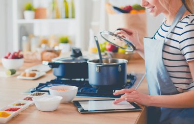 Mutfakta yemek yapmak için tablet bilgisayar kullanan genç bir kadın.