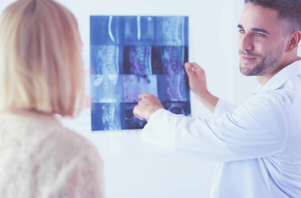 Красивый врач разговаривает с молодой пациенткой и делает заметки, сидя в своем кабинете.