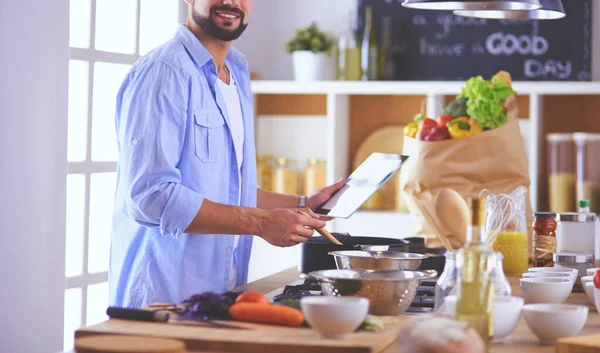 Man following recipe on digital tablet and cooking tasty and healthy food in kitchen at home