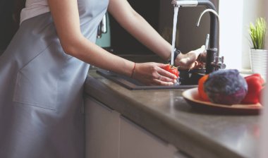 Mutfak lavabosunda domates yıkayan bir kadın.