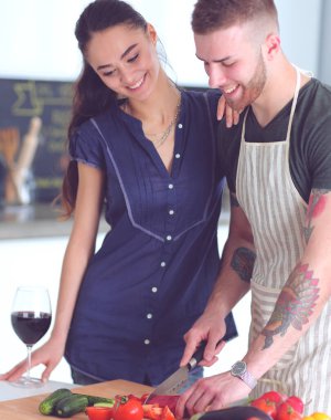 Sebze doğrayan genç bir adam ve mutfakta dizüstü bilgisayarı olan bir kadın.