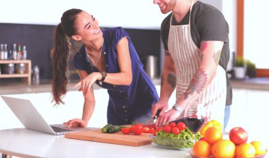 Sebze doğrayan genç bir adam ve mutfakta dizüstü bilgisayarı olan bir kadın.