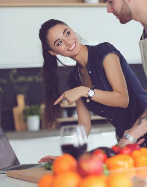 Sebze doğrayan genç bir adam ve mutfakta dizüstü bilgisayarı olan bir kadın.