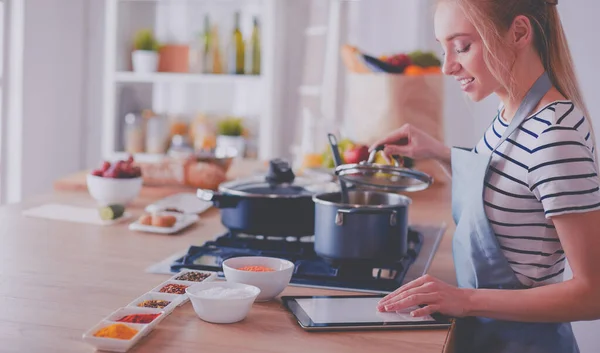 Mujer joven usando una tableta para cocinar en su cocina — Foto de Stock