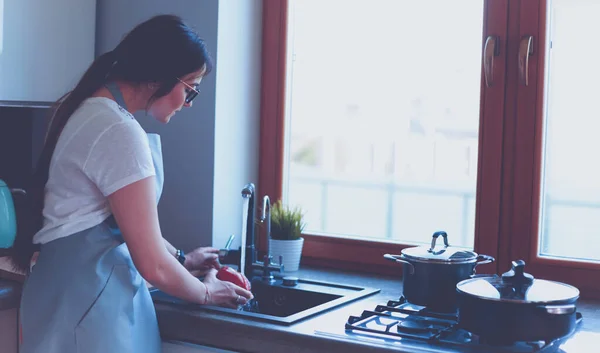 Γυναίκα πλένει λαχανικά. Όμορφη νεαρή γυναίκα πλένει λαχανικά για σαλάτα και χαμογελά ενώ στέκεται στην κουζίνα — Φωτογραφία Αρχείου