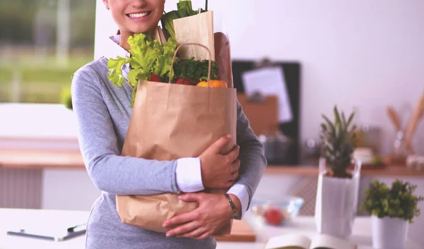 Sebzeli alışveriş poşeti taşıyan genç bir kadın mutfakta duruyor.. — Stok fotoğraf
